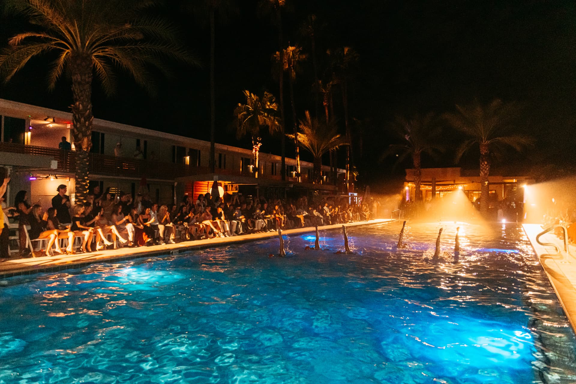 Synchronized swimmers performing in the glowing pool at The Pool Club, Hotel Adeline, as guests line the deck