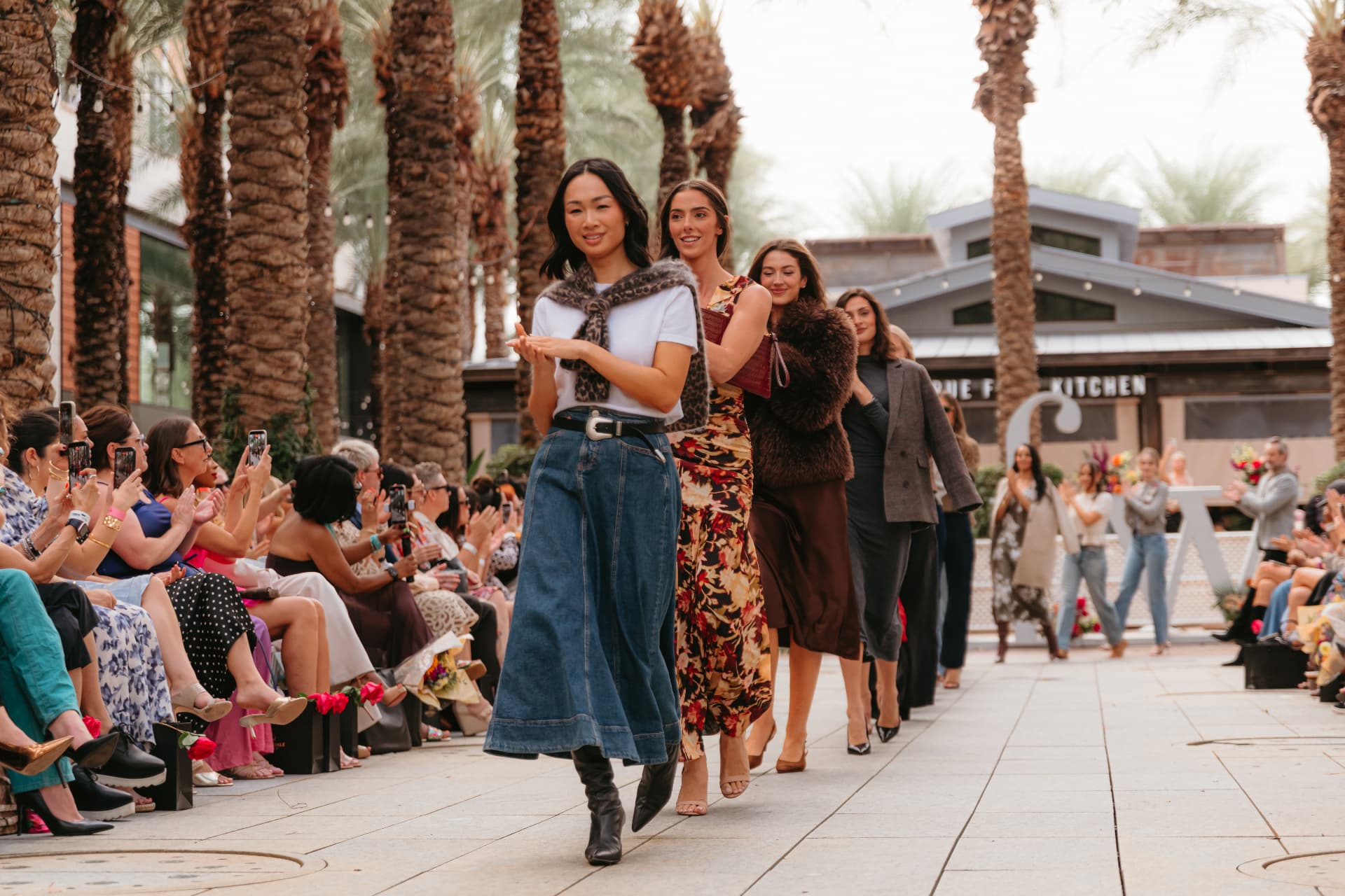 Models walking the palm-lined runway at the Scottsdale Fashion Week Finale as guests film from the front row
