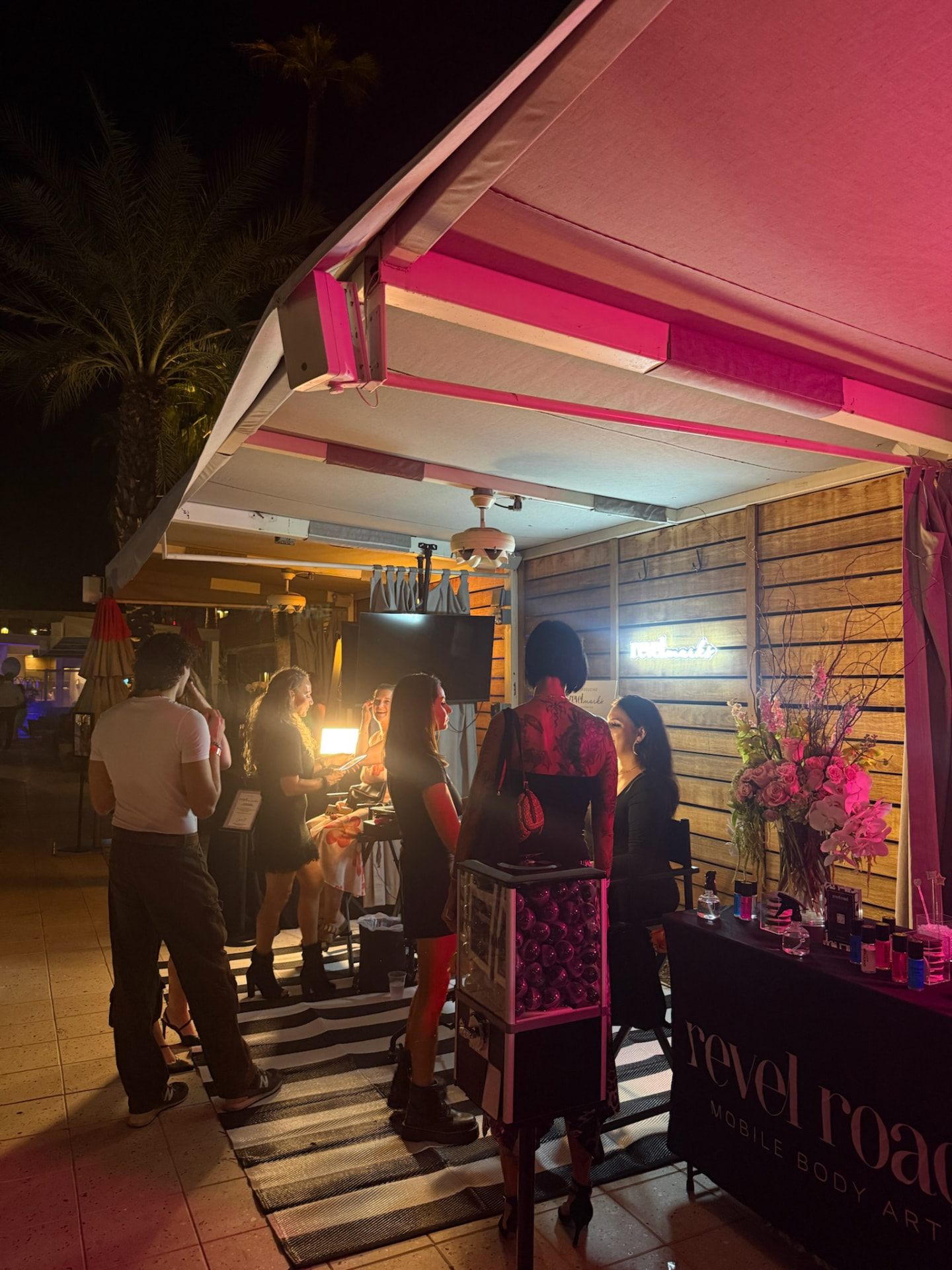 Revel Road's poolside cabana setup with Artists, guests, branded rug, tattoo capsule machine and styling table