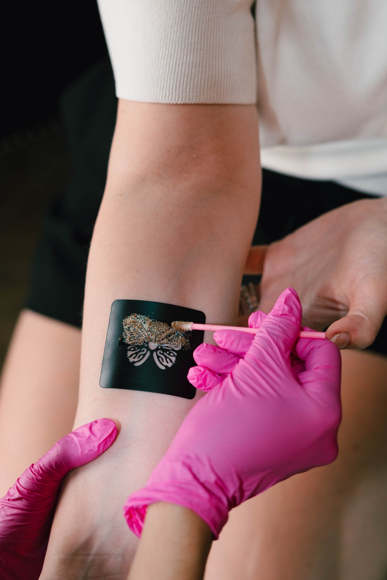 Artist applying a custom glitter temporary tattoo to a guest's arm
