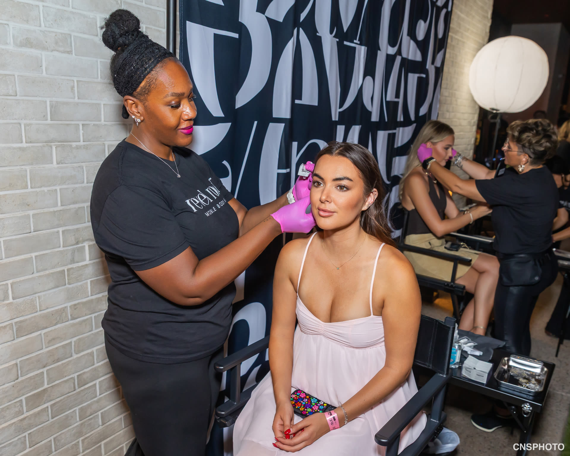 Revel Road Artist styling a guest in a pink dress beside the lettered backdrop at the Kickoff