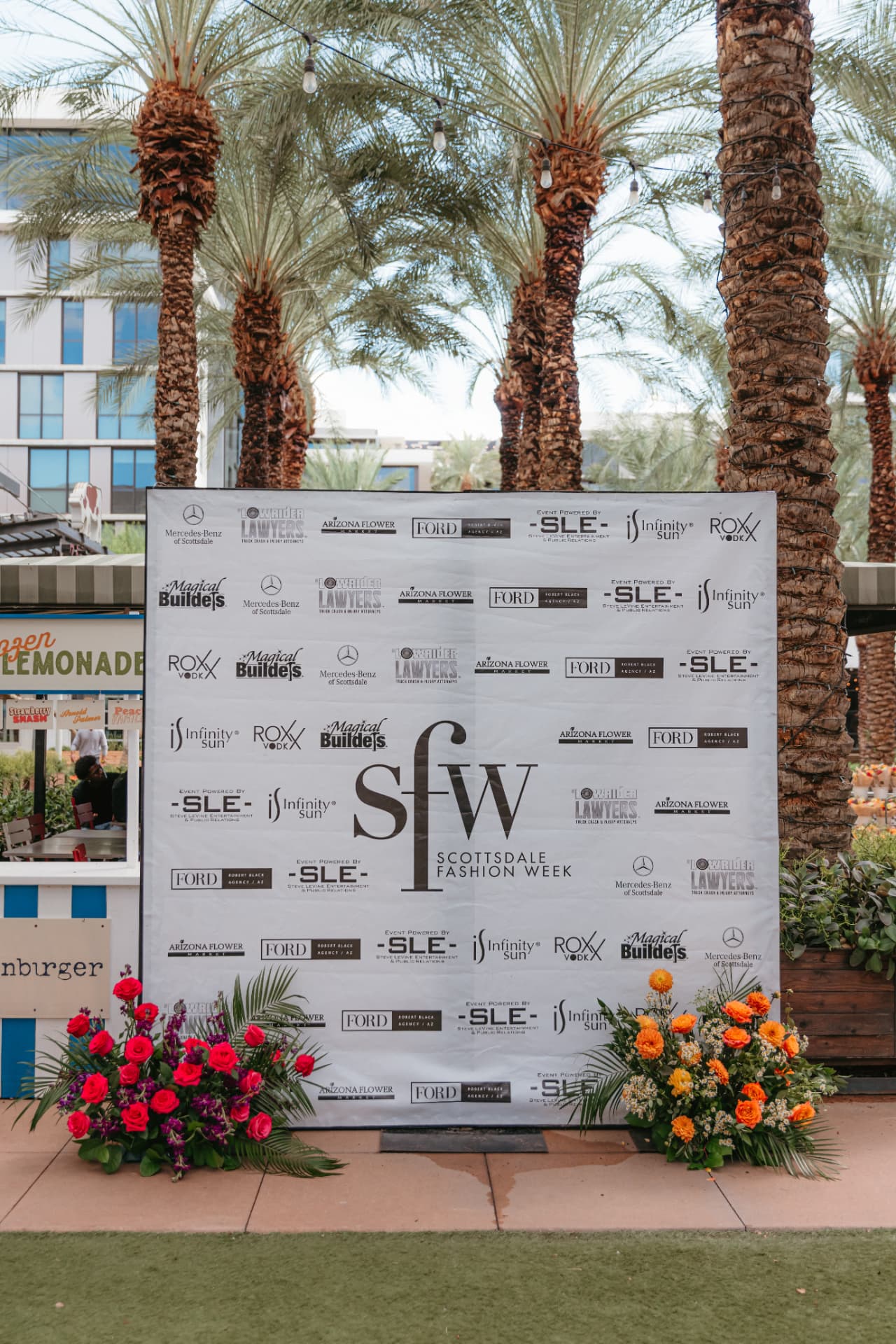 Scottsdale Fashion Week sponsor backdrop framed by flowers and palm trees